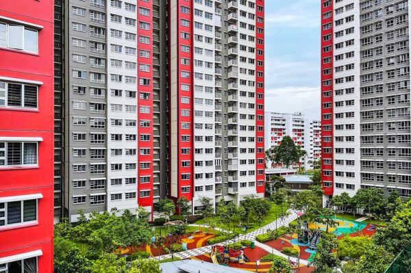 High-rise residential buildings with red and white facades surround a colorful playground and garden space. The atmosphere is lively and communal.