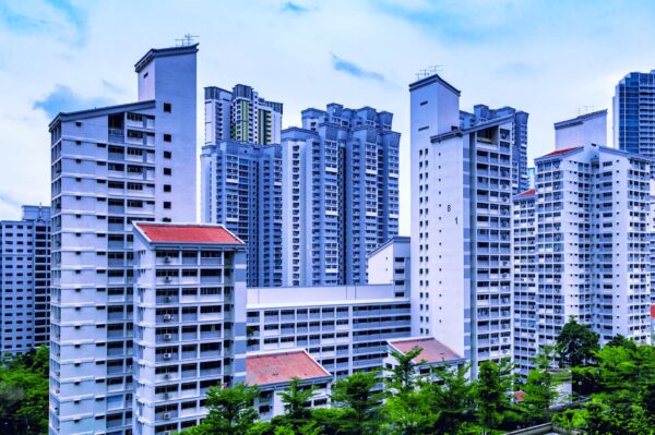 A cluster of tall, white high-rise apartment buildings with red roofs under a blue sky, surrounded by green trees, conveying urban density.