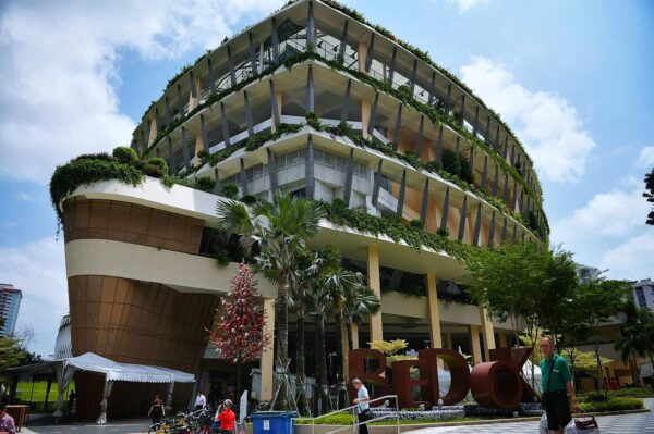 A modern, eco-friendly building with lush vertical gardens and multiple tiers. It has an inviting, green atmosphere under a clear, sunny sky.