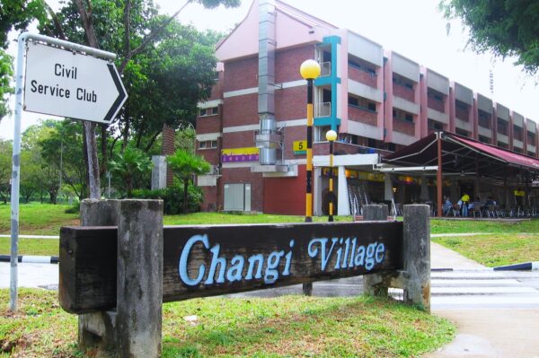 Sign reading "Changi Village" in front of a multi-story building with a covered outdoor seating area. A sign points toward the Civil Service Club.
