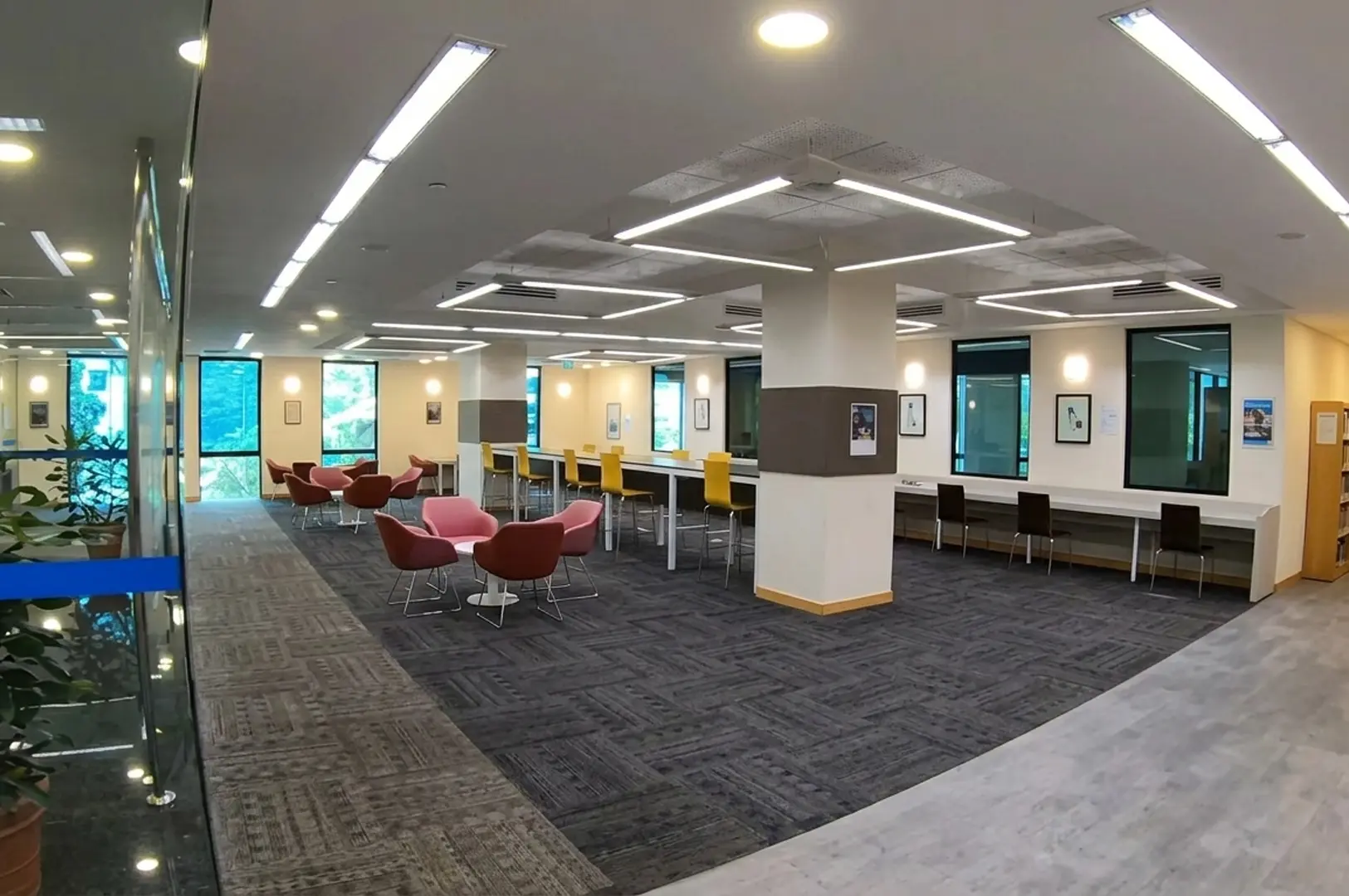 Modern study area featuring pink and yellow chairs long tables and geometric ceiling lights
