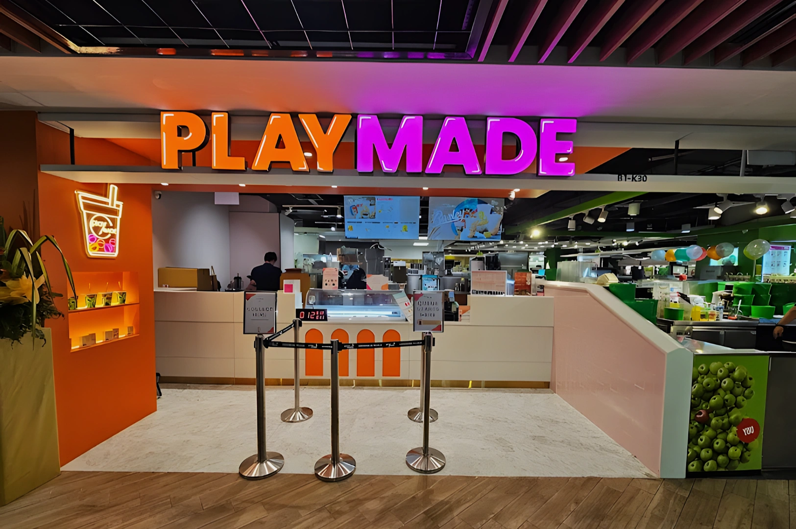 Colorful storefront of a bubble tea shop named Playmade. Bright orange and pink signage with a modern, inviting interior. People inside preparing drinks.