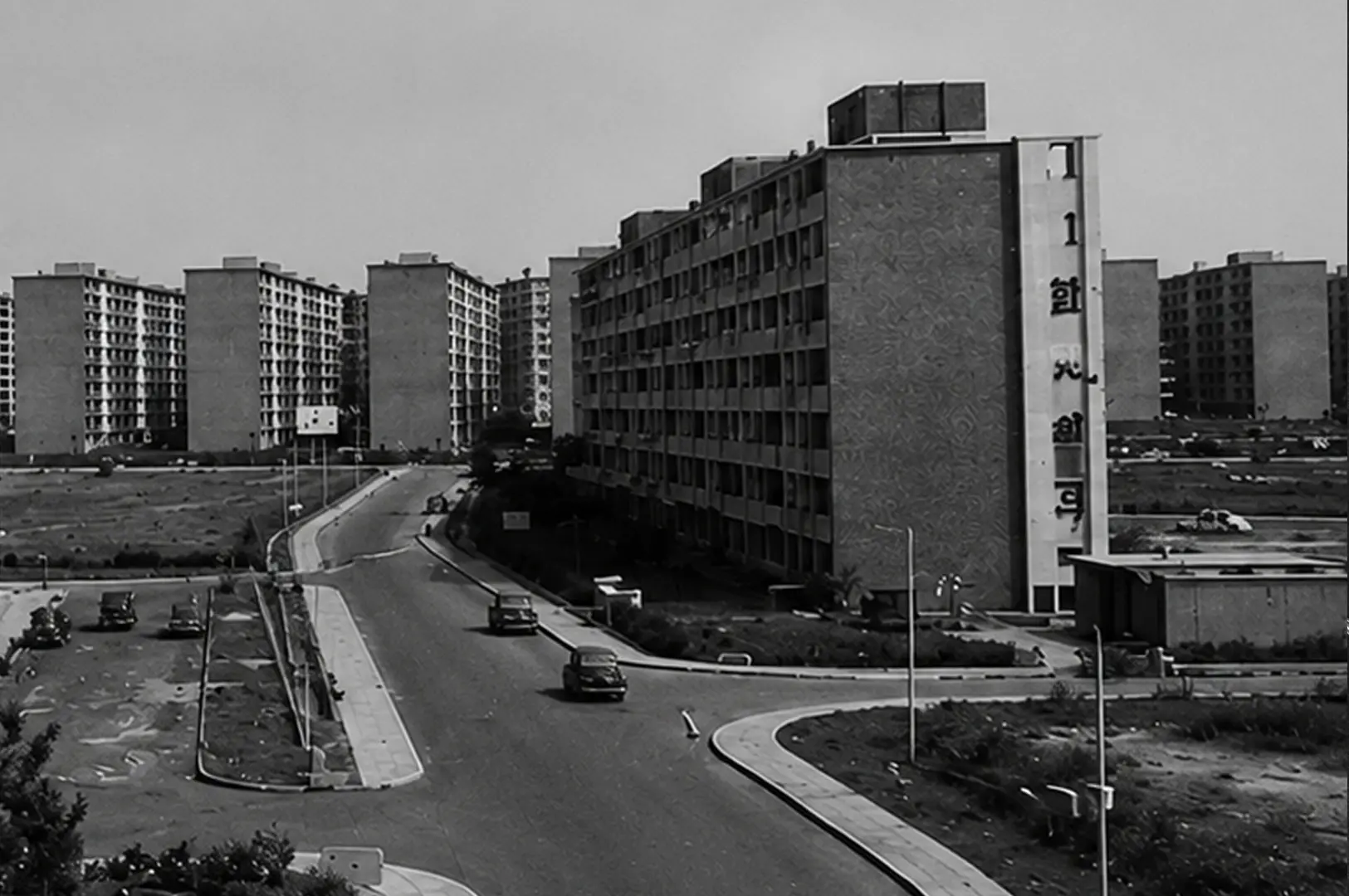 Black and white view of early Queenstown HDB flats with vintage cars on a winding road and undeveloped land