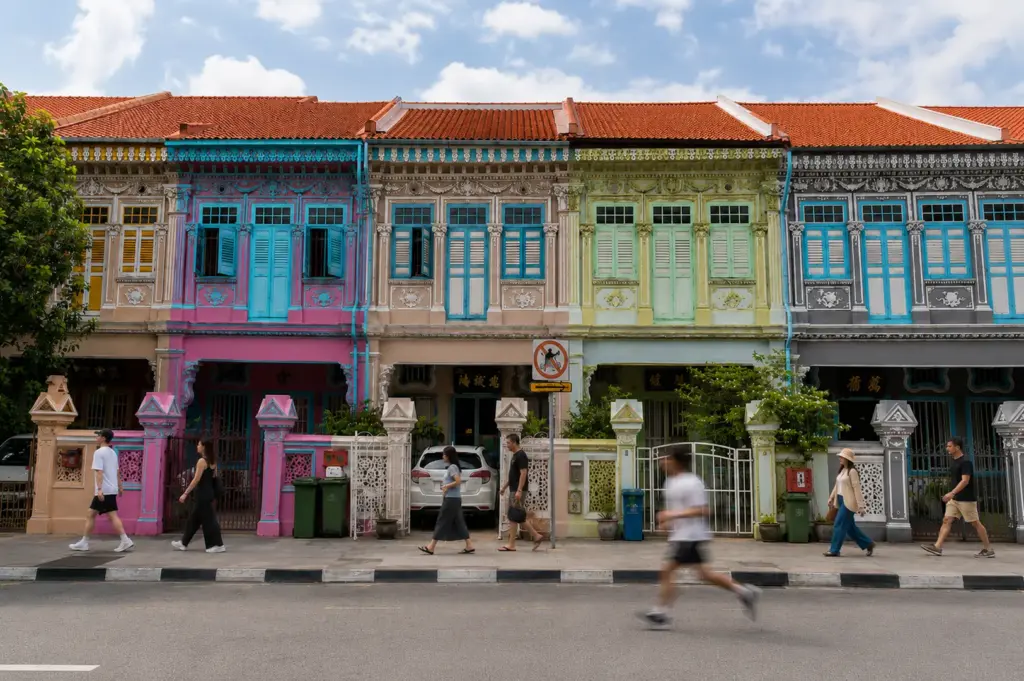 Row of colorful Peranakan shophouses in Katong featuring pastel pink, blue, green, and grey facades with ornate architectural details and pedestrians walking by