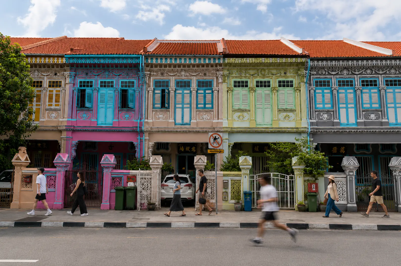 Row of colorful Peranakan shophouses in Katong featuring pastel pink, blue, green, and grey facades with ornate architectural details and pedestrians walking by