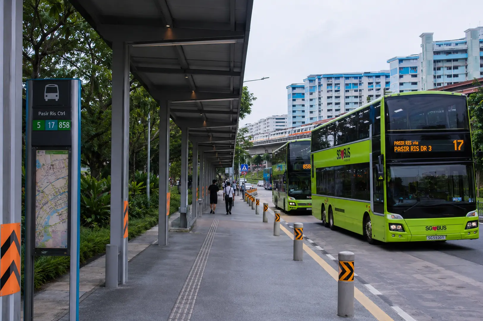 Green double-decker buses at a covered bus stop with HDB flats and MRT tracks in the background