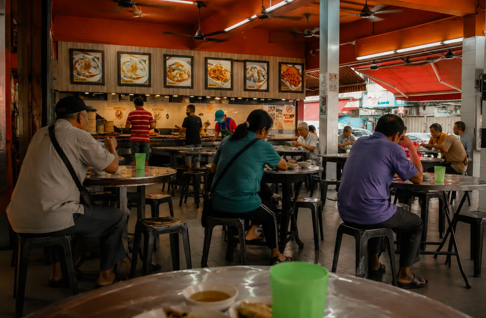 Diners seated at round tables in a local vegetarian eatery with orange ceiling and framed food pictures displayed above the counter.