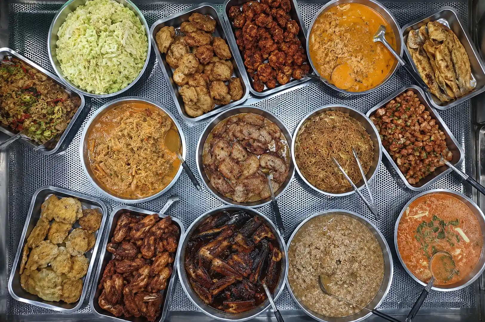 Top-down view of a zi char stall display featuring various dishes like fried chicken, braised pork, curry, and vegetables in metal trays