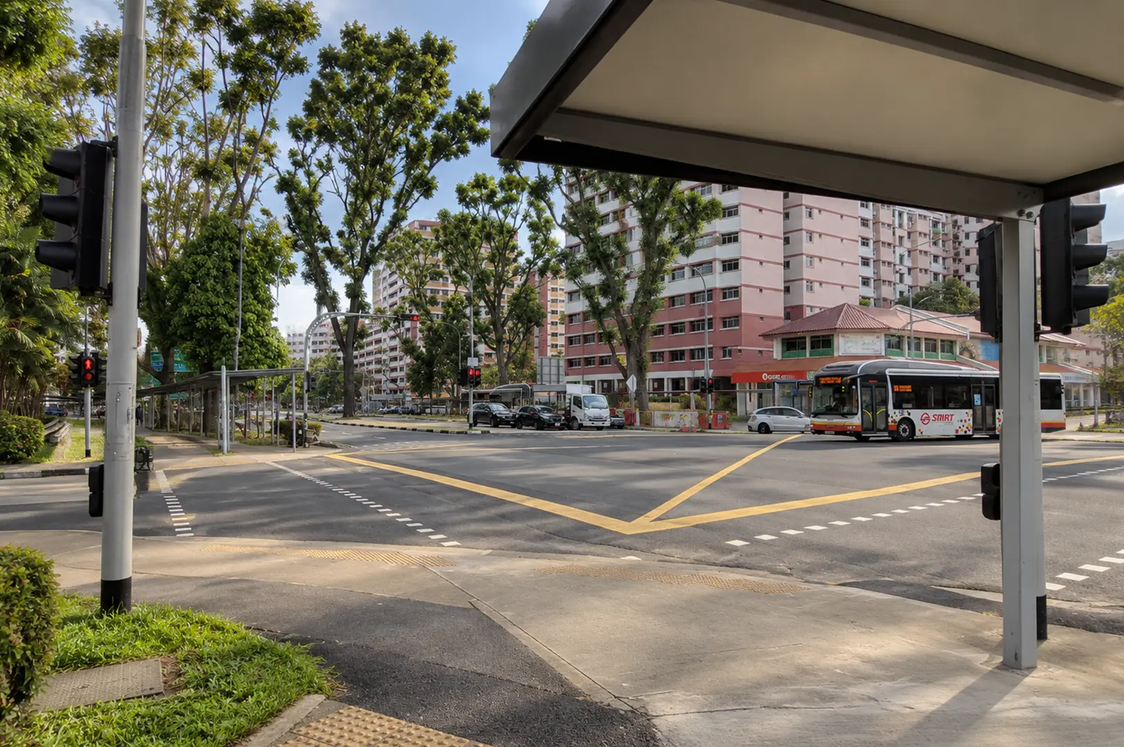 A sunny Choa Chu Kang street with HDB flats, buses, mature trees, and a busy road junction.