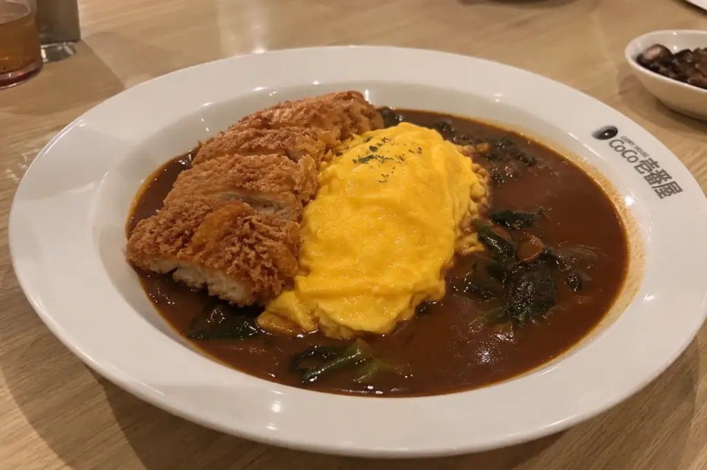 Plate of crispy chicken cutlet and fluffy omelette served with dark curry sauce at a CoCo Ichibanya restaurant.