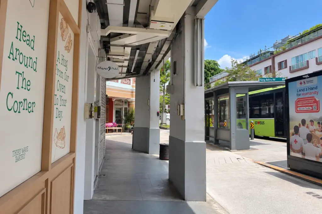 Tiong Bahru streetscape with a bus stop, heritage shophouses, and a Third Wave Bakery storefront under a covered walkway.