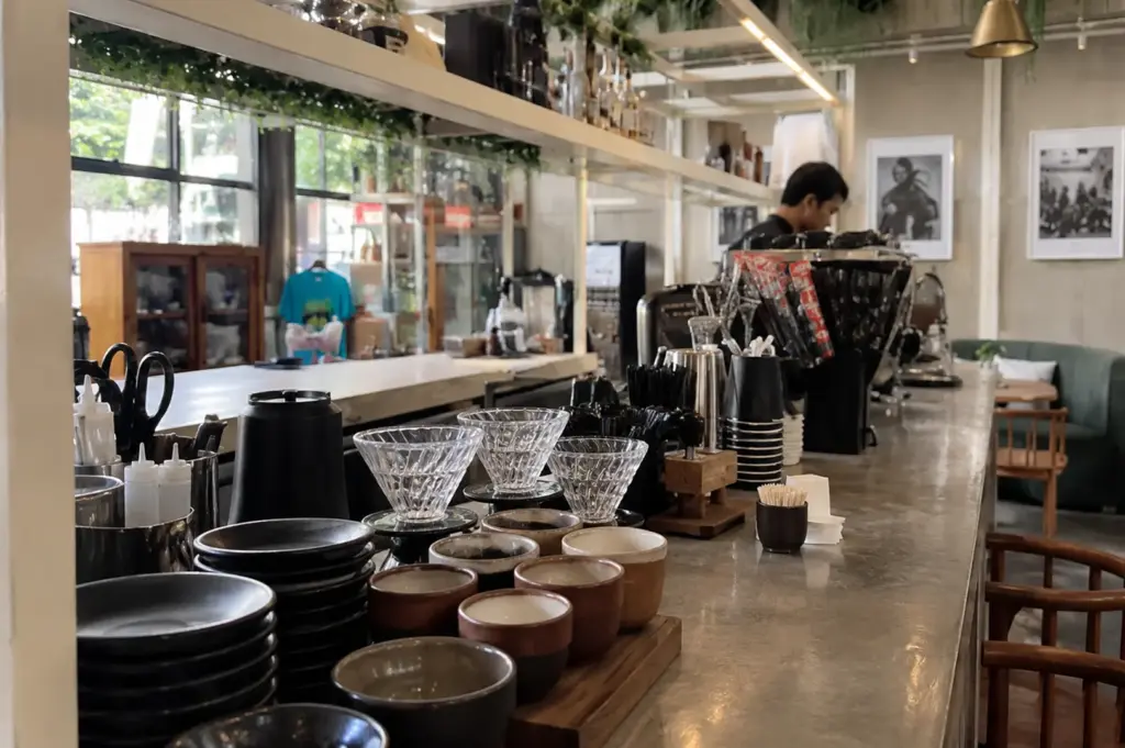 Modern café interior featuring a coffee bar with pour-over equipment, cozy seating, and natural daylight streaming through large windows.