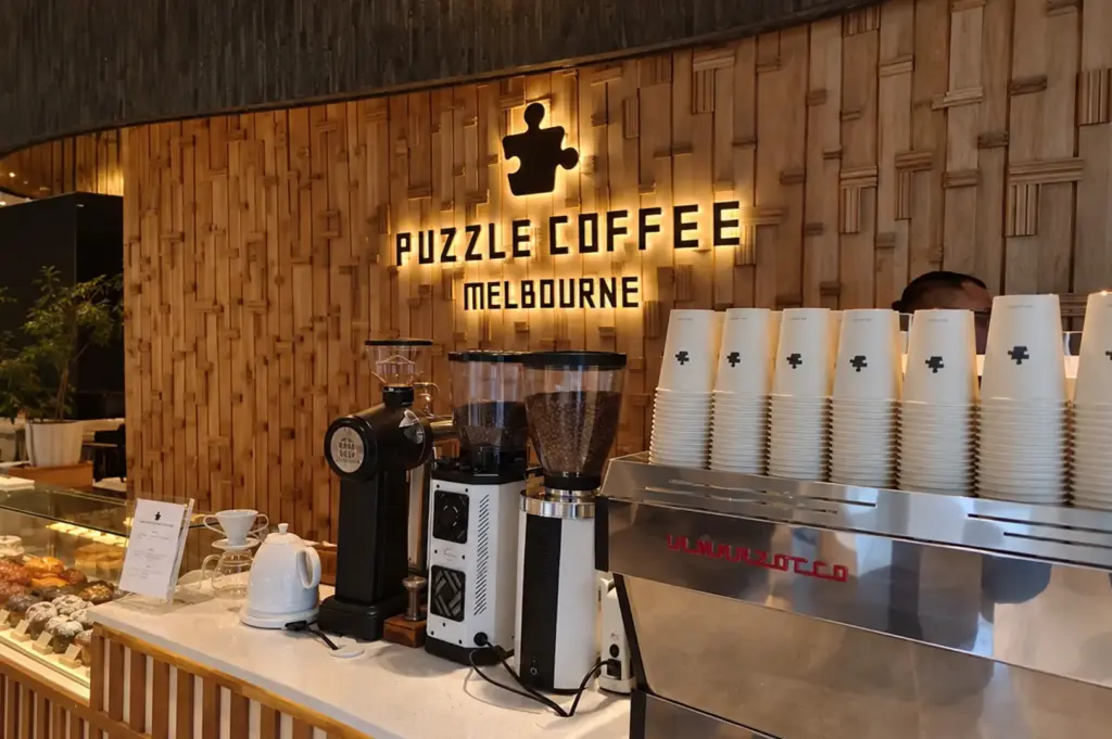 Warm interior of Puzzle Coffee with wooden walls, coffee equipment, and neatly stacked cups.